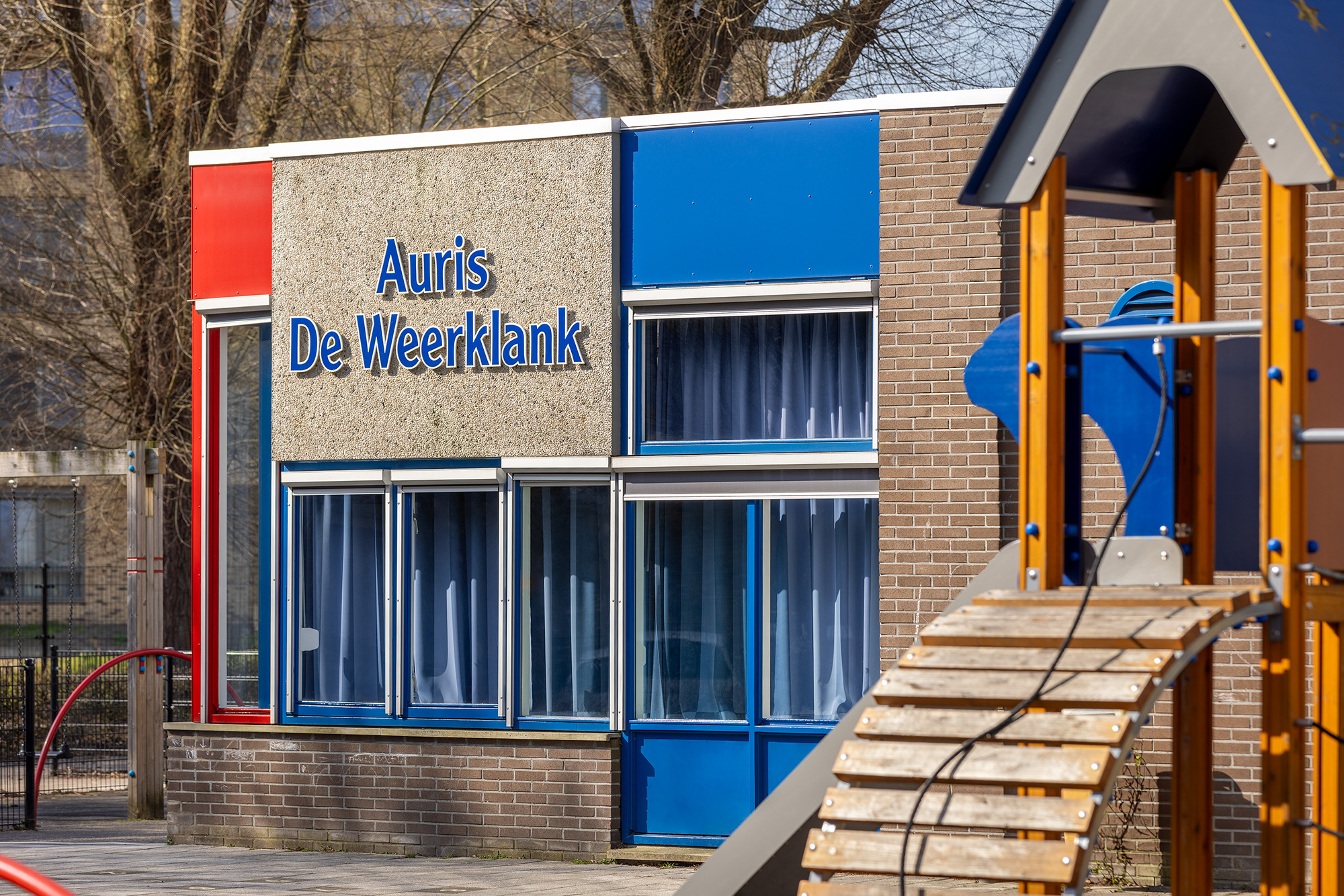 Buitenkant van het schoolgebouw van Auris De Weerklank met speeltoestel op de voorgrond.