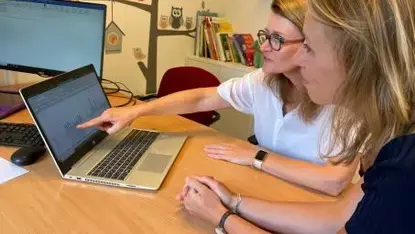 Twee vrouwen wijzen naar een scherm