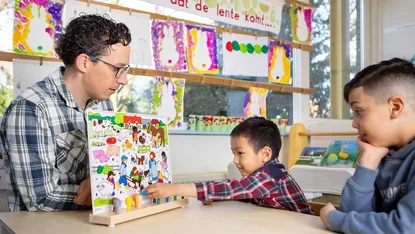 Leerkracht werkt met twee jongens aan een taaloefening met een prentenboek.