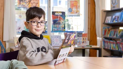 Jongen met bril leest een boek in de schoolbibliotheek.