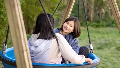 Twee meisjes schommelen samen lachend in een nestschommel.