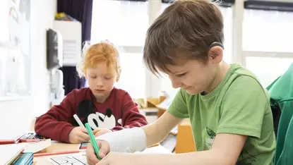 Een leerling met hoortoestel schrijft aan zijn tafel in de klas.