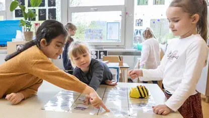 Drie leerlingen doen een proefje met een programmeerbare bij op tafel.