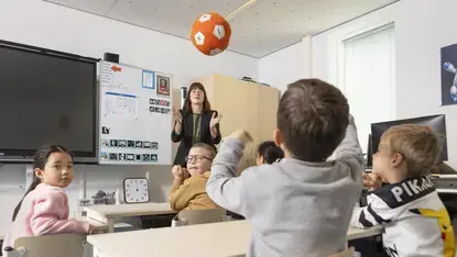 Leerkracht gooit een bal met rekentekens terwijl een groep leerlingen reageert in de klas.