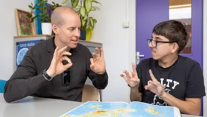Een docent en een leerling gebruiken gebarentaal terwijl ze een atlas bekijken.