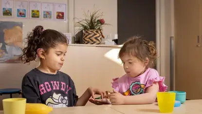 Twee leerlingen met hoortoestellen delen iets aan tafel.