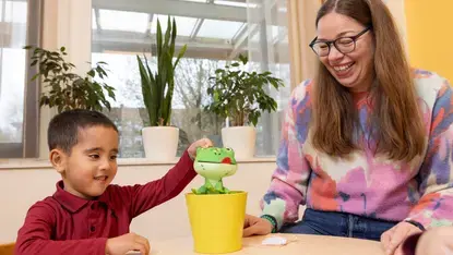 Een begeleider laat een pluchen kikker zien aan een leerling tijdens een taaloefening.