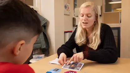 Een leerkracht legt woordkaarten en blokjes uit aan een leerling.