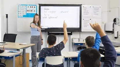 Leerkracht bespreekt een dictee met de klas, leerlingen steken hun vinger op