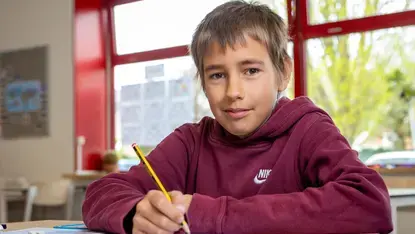 Een leerling schrijft aan zijn tafel in de klas.