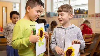 Twee leerlingen laten elkaar hun knutselwerk van een zonnebloem zien.