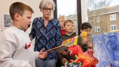 Een begeleider laat een boek en speelgoeddinosaurussen zien aan een groep leerlingen.