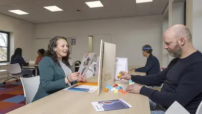 Een vrouw en een man spelen met bouwstenen aan een tafel met een bordje 'Auris Cursuscentrum'.