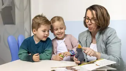Een vrouw laat twee kinderen een knuffeldier en een prentenboek zien.