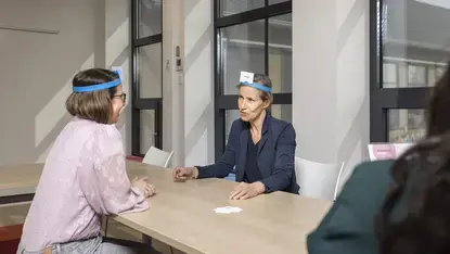 Twee vrouwen doen een raadspel met kaarten op een blauwe hoofdband.