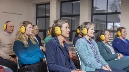 Een groep collega's met gele gehoorbeschermers luistert tijdens de cursus Ervaar Gehoorverlies..