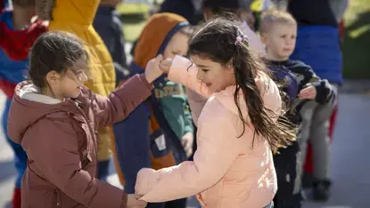 Twee meisjes stoten hun ellebogen tegen elkaar buiten, tussen andere kinderen.