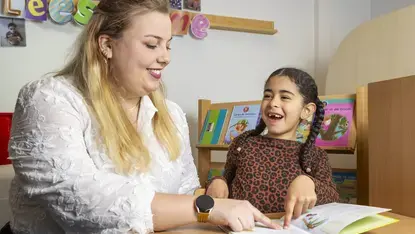 Een logopedist leest samen met een meisje in een boek. Ze wijzen allebei naar de tekst.