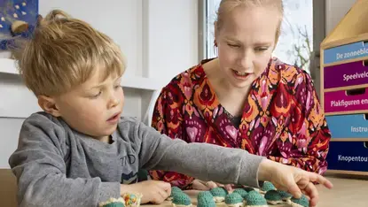 Een logopedist en een jongen leggen samen gehaakte schildpadjes op een rij.