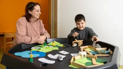 Leerkracht kijkt toe terwijl een leerling op de speeltafel met letterkaartjes en figuurtjes speelt.