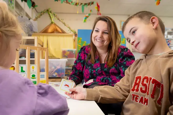 Leerkracht werkt met twee kinderen aan een taal- of spraakoefening met beeldkaarten.