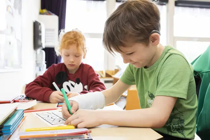 Een leerling met hoortoestel schrijft aan zijn tafel in de klas.