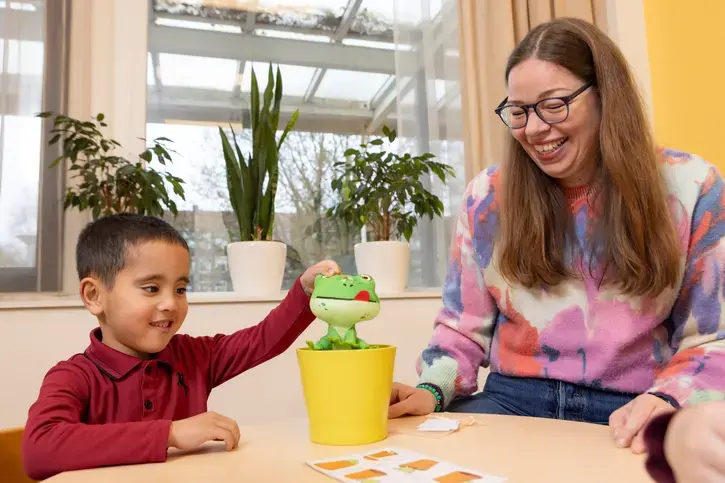 Een begeleider laat een pluchen kikker zien aan een leerling tijdens een taaloefening.