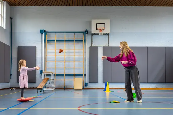 Een leerling vangt een zakje terwijl ze op een balanceerkussen staat, in de gymzaal.