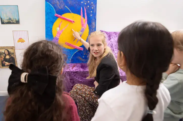 Een begeleider wijst iets aan op een schilderij, terwijl leerlingen luisteren.
