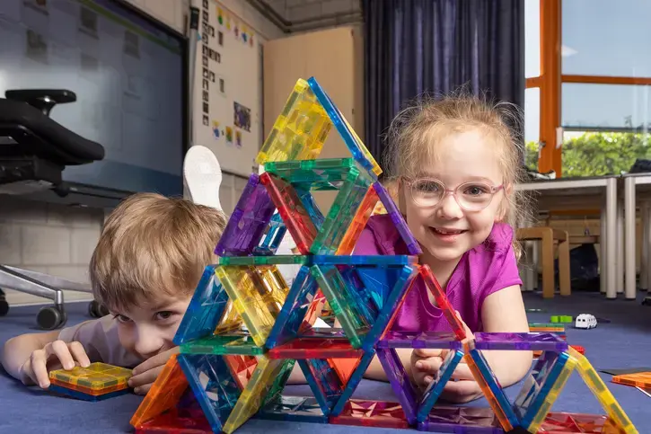 Twee kinderen liggen op de grond achter een piramide van gekleurde magnetische bouwstenen.