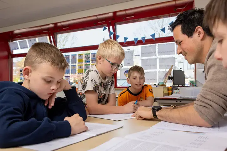 Een leerkracht helpt drie jongens aan tafel met hun schoolwerk.