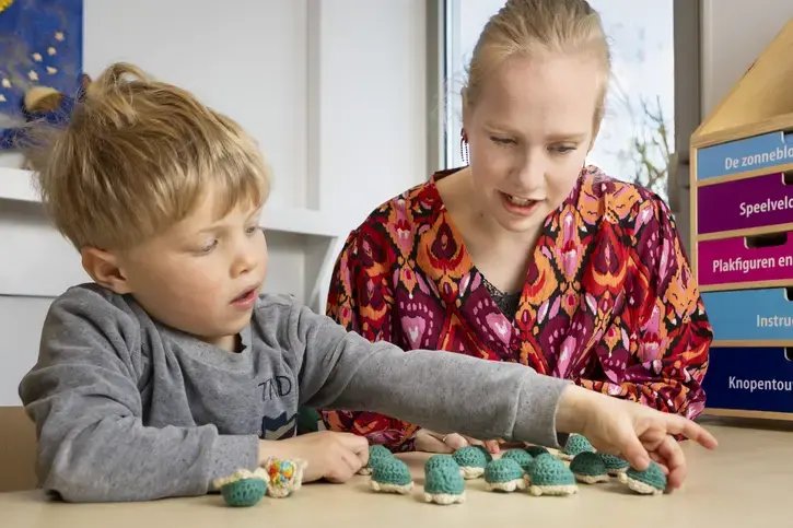 Een logopedist en een jongen leggen samen gehaakte schildpadjes op een rij.