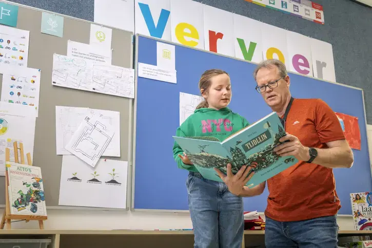 Een begeleider leest samen met een leerling voor uit een boek over de tijdlijn.