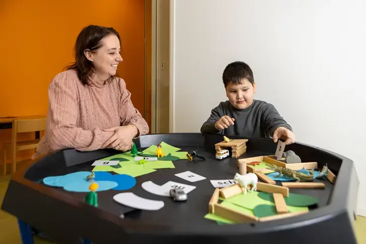 Leerkracht kijkt toe terwijl een leerling op de speeltafel met letterkaartjes en figuurtjes speelt.