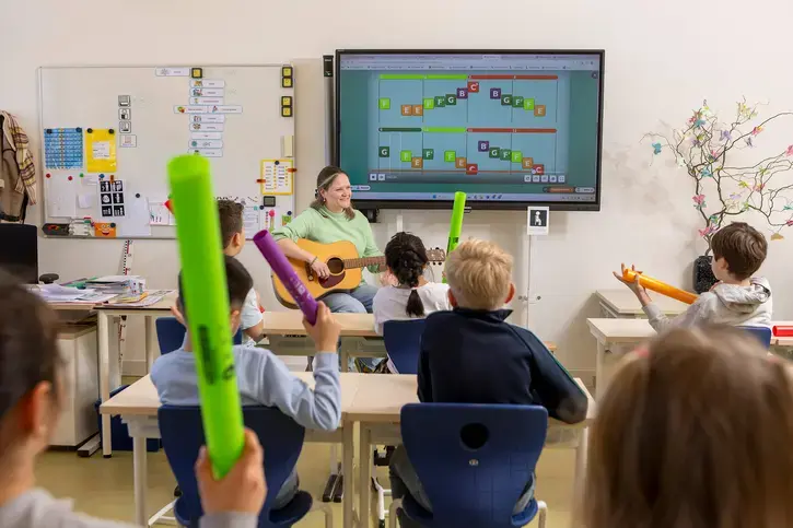 Leerkracht speelt gitaar voor een groep leerlingen die meedoen met klankbuisjes tijdens een taalactiviteit.