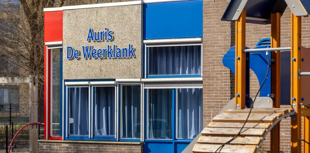 Buitenkant van het schoolgebouw van Auris De Weerklank met speeltoestel op de voorgrond.