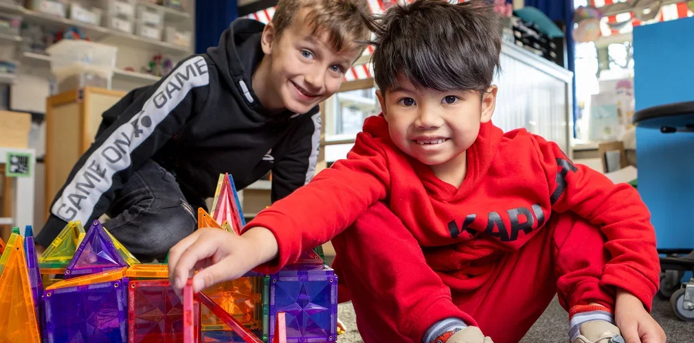 Twee jongens bouwen lachend samen met magnetische bouwstenen.