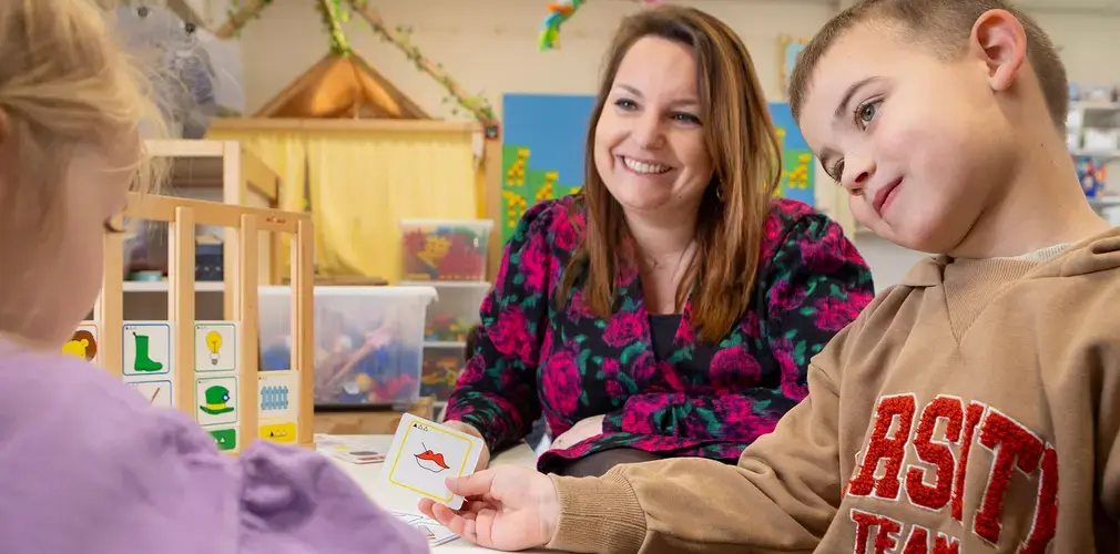 Leerkracht werkt met twee kinderen aan een taal- of spraakoefening met beeldkaarten.
