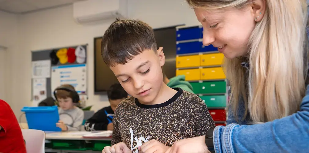 Leerkracht helpt een leerling individueel bij een schrijfopdracht in de klas.