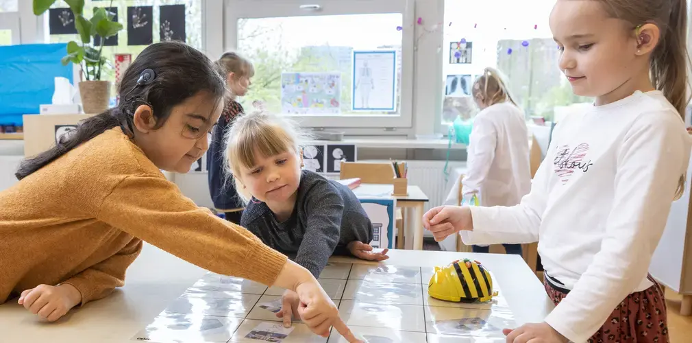 Drie leerlingen doen een proefje met een programmeerbare bij op tafel.