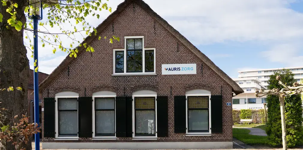 Vooraanzicht van locatie met een puntdak en een bord met Auris Zorg