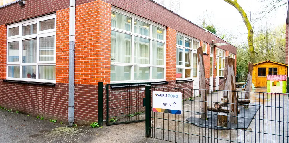 Een hek met een gebouw en een bordje met Auris Zorg