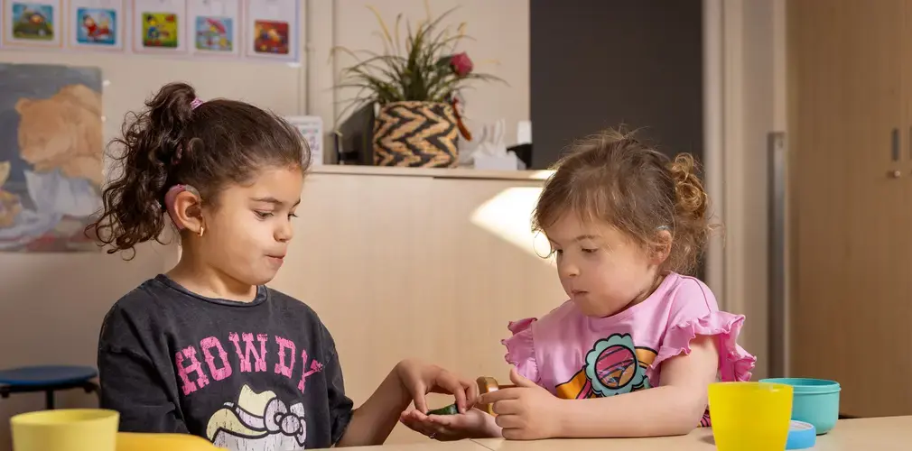 Twee leerlingen met hoortoestellen delen iets aan tafel.