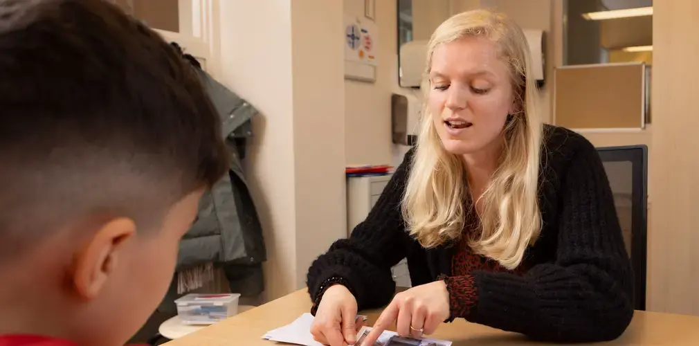 Een leerkracht legt woordkaarten en blokjes uit aan een leerling.