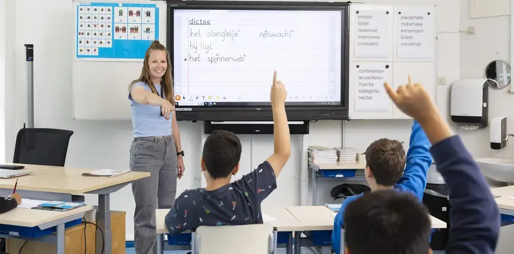 Leerkracht bespreekt een dictee met de klas, leerlingen steken hun vinger op