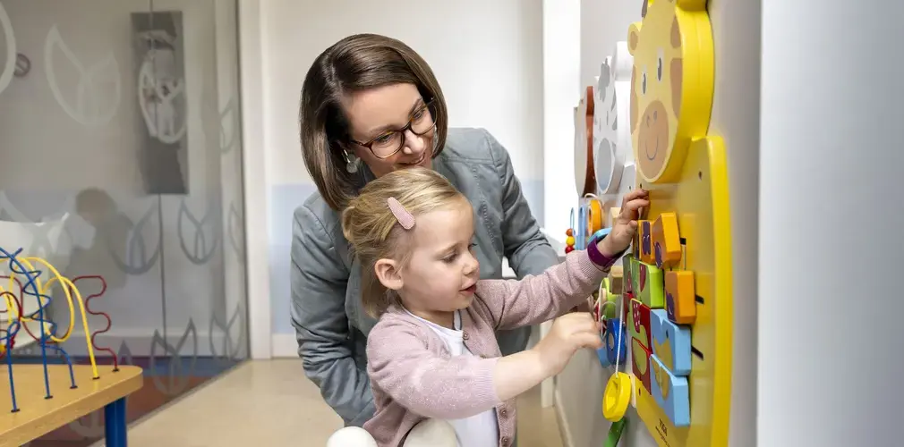 Een vrouw helpt een peuter met een kleurrijk wandspeelgoed met een giraffe.Een vrouw helpt een peuter met een kleurrijk wandspeelgoed met een giraffe.