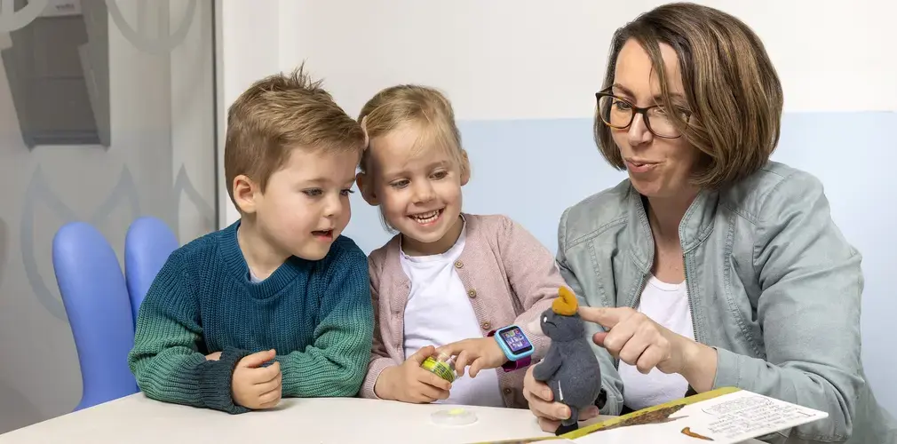 Een vrouw laat twee kinderen een knuffeldier en een prentenboek zien.
