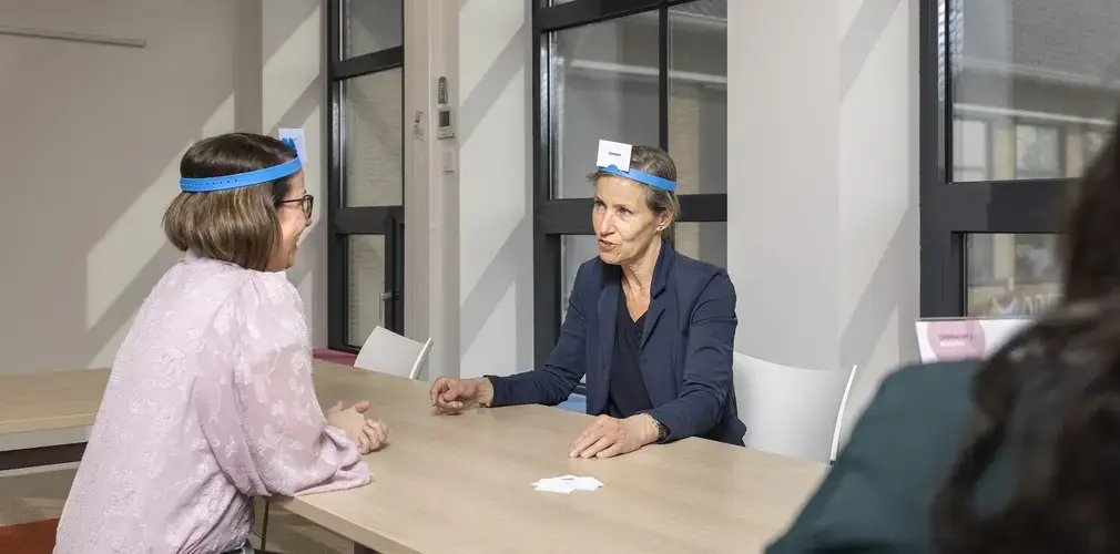 Twee vrouwen doen een raadspel met kaarten op een blauwe hoofdband.