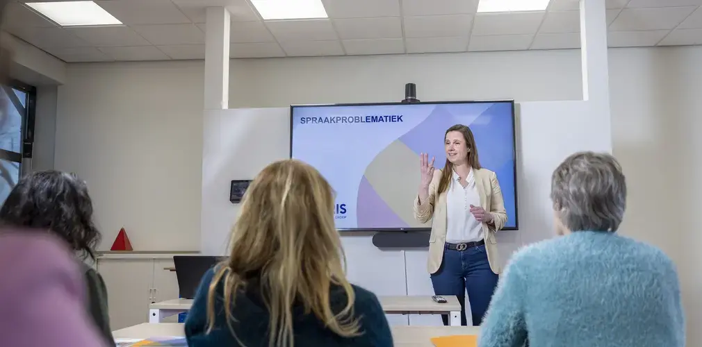 Een vrouw geeft een presentatie over spraakproblematiek voor een groep collega's.
