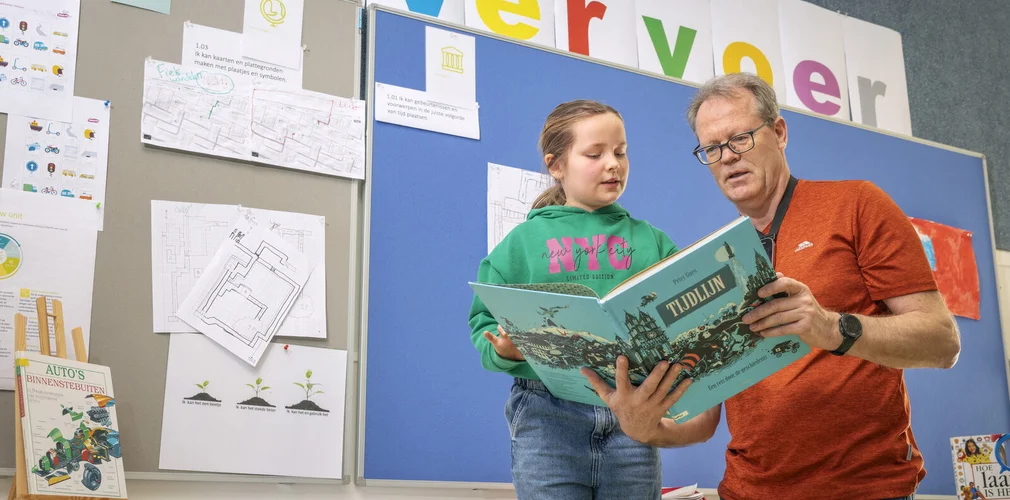 Een begeleider leest samen met een leerling voor uit een boek over de tijdlijn.